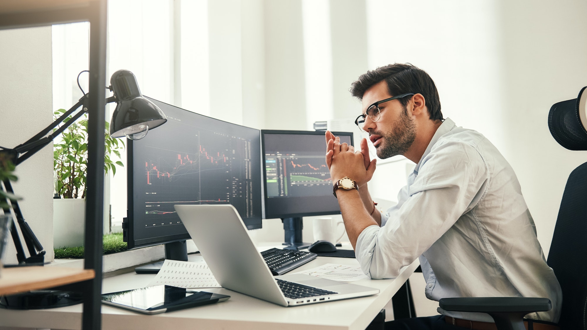 Trading strategy. Successful young trader in eyeglasses looking at analyzing trading charts on
